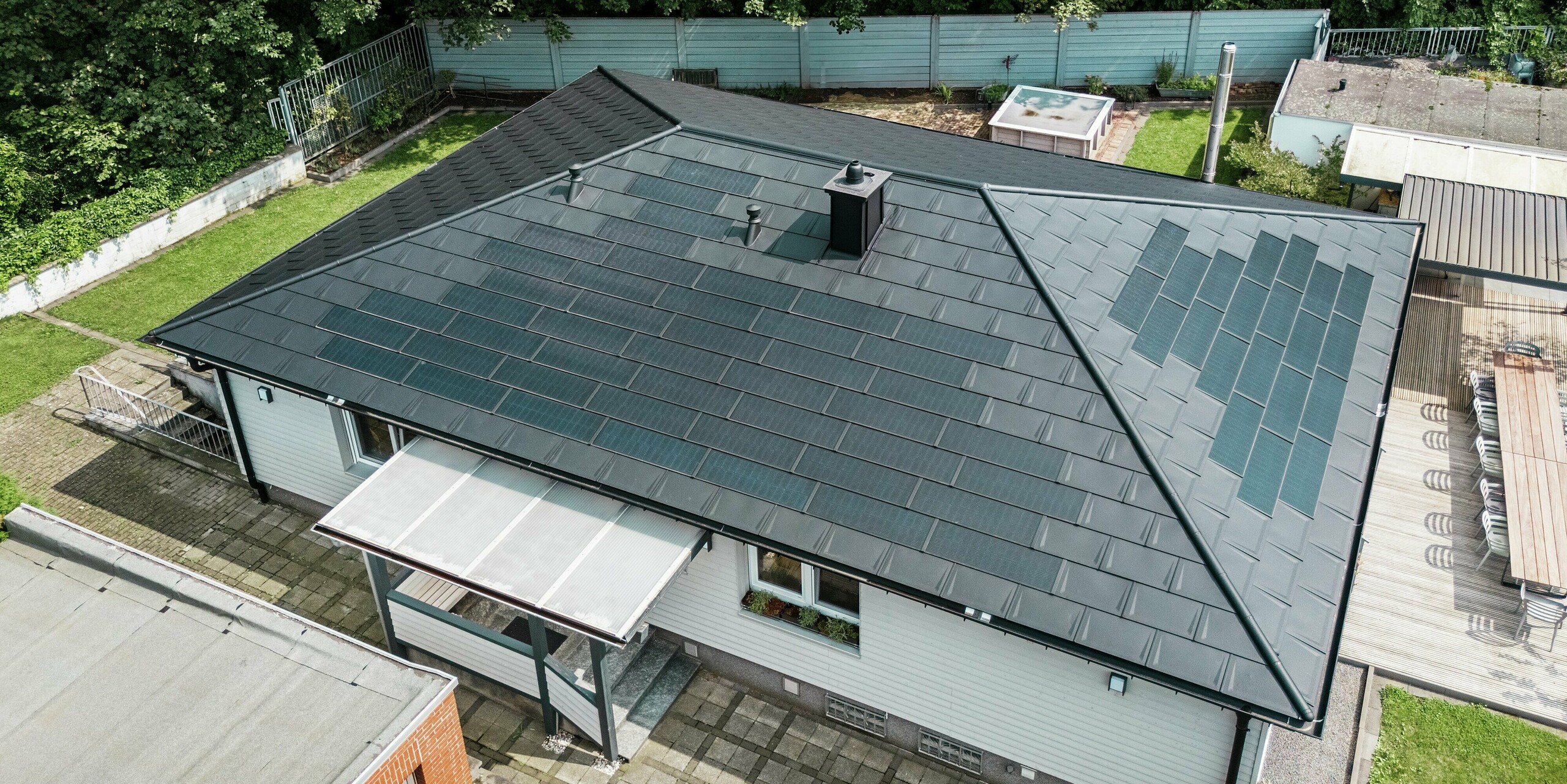 Bungalow moderne à Rommerskirchen avec toit en aluminium PREFA. Les tuiles solaires innovantes PREFA protègent la maison et produisent en même temps de l'électricité à partir de l'énergie solaire durable. Les R.16 offrent une protection supplémentaire. Le système d'évacuation des eaux pluviales avec la gouttière et tuyau de descente assure la fonctionnalité nécessaire. Tous les produits en aluminium PREFA sont dotés d'un revêtement de couleur P.10 noir de haute qualité, garantissant ainsi une apparence générale élégante.