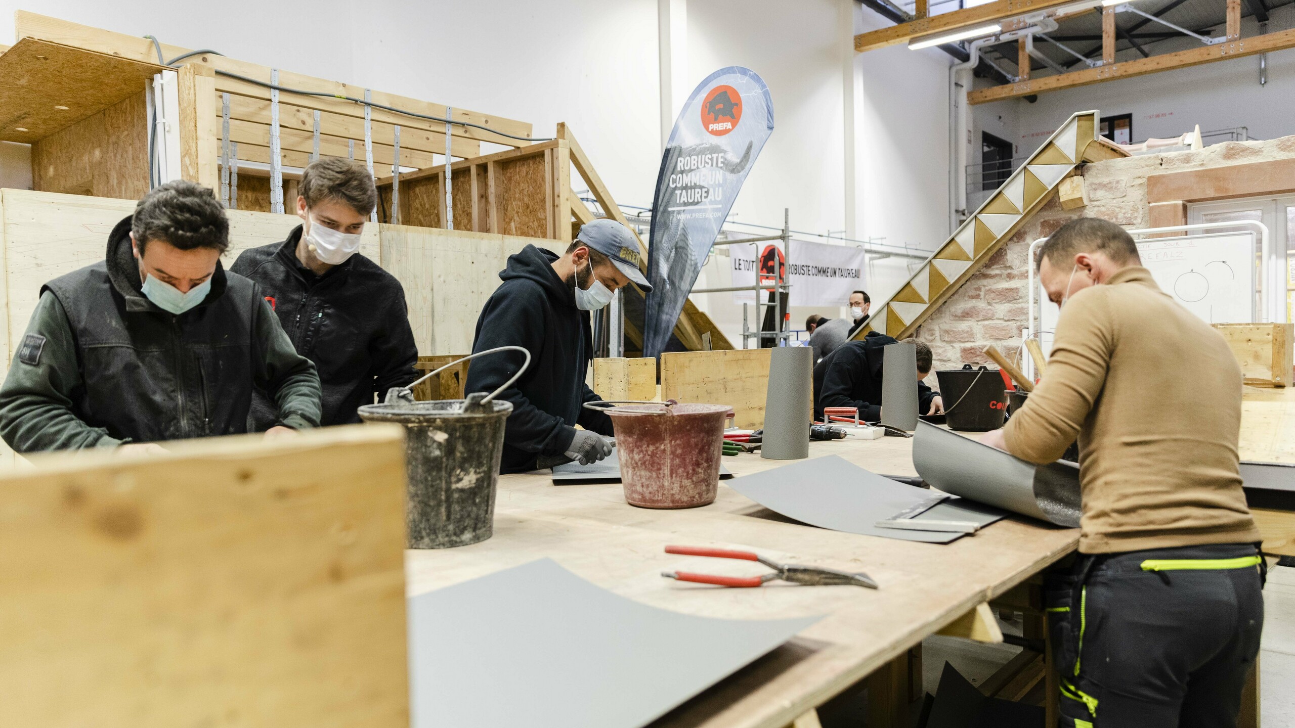 Des participants portant des masques travaillent sur des tables dans un atelier de formation, manipulant divers outils et matériaux.