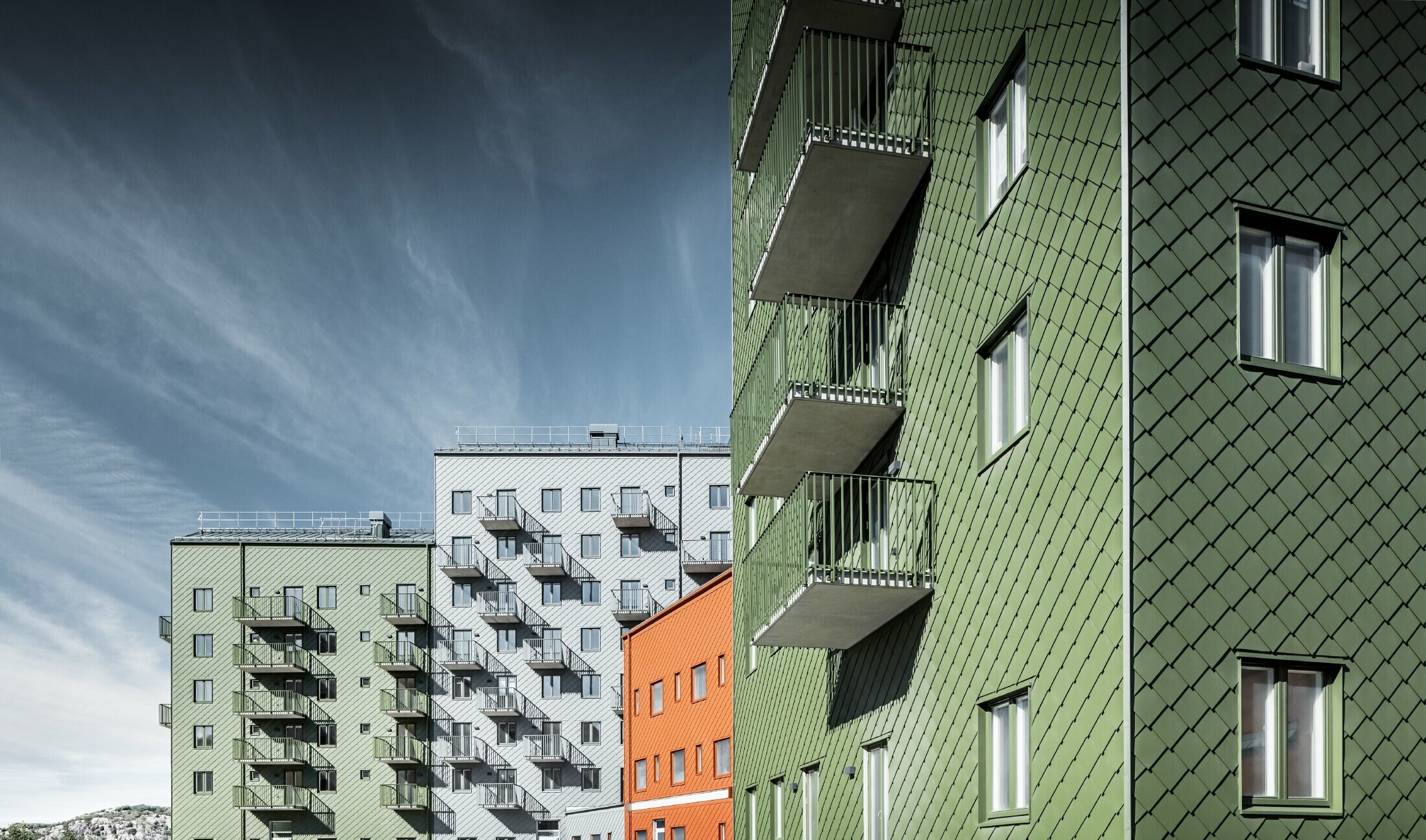 Plusieurs bâtiments d’habitation les uns à côté des autres, recouverts de losanges de façade 29 × 29 PREFA dans les teintes rouge tuile, vert olive et gris souris.