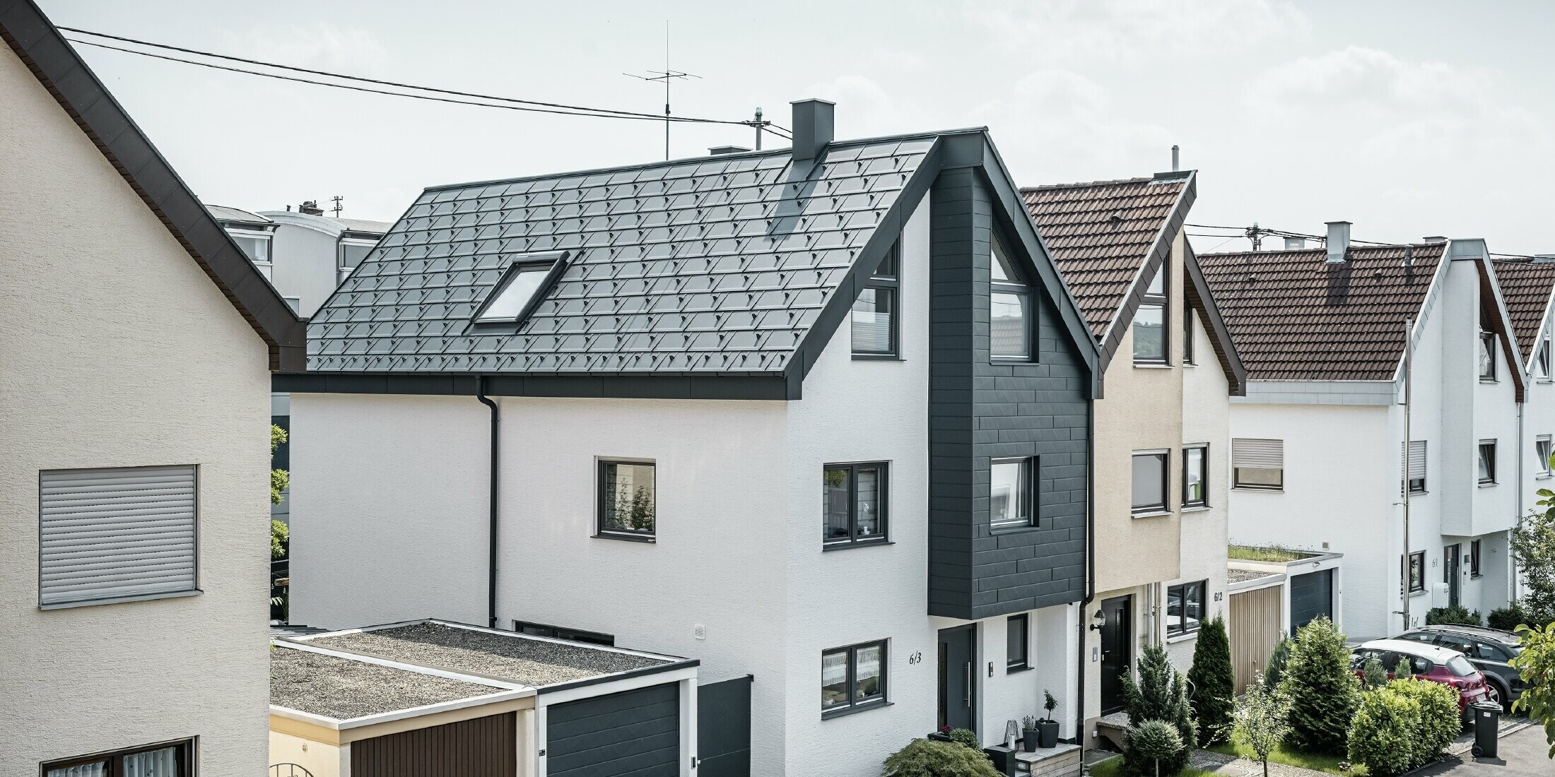 La moitié d'une maison jumelée a déjà été rénovée, avec une façade fraîchement crépie de blanc, combinée à une façade avec Siding.X PREFA en anthracite. Le toit est recouvert du R.16 PREFA. L'écoulement des eaux de pluie se fait par la gouttière carrée et le tuyau de descente PREFA.