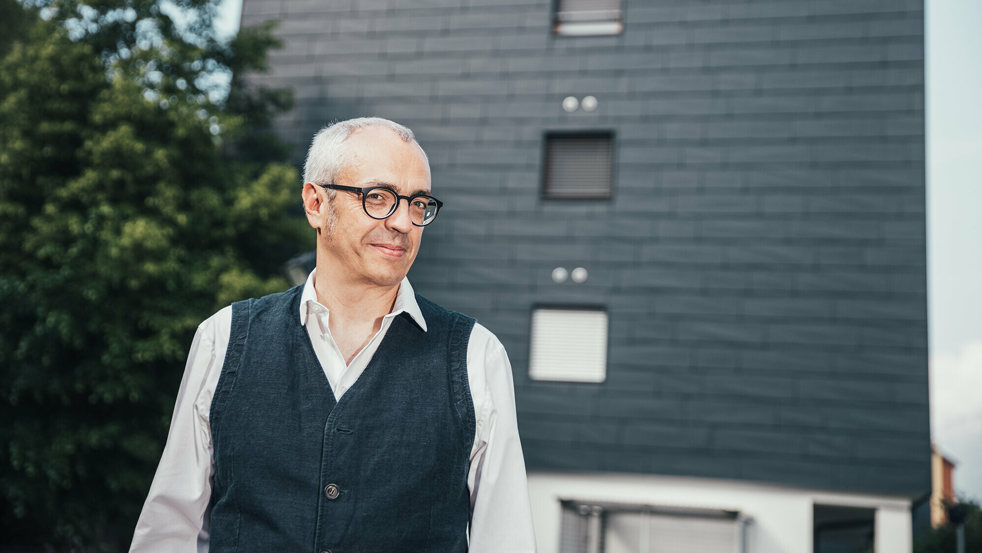 Portrait de l'architecte Manuel Benedikter devant l'immeuble après la rénovation thermique grâce à la façade Prefa dans la teinte anthracite.