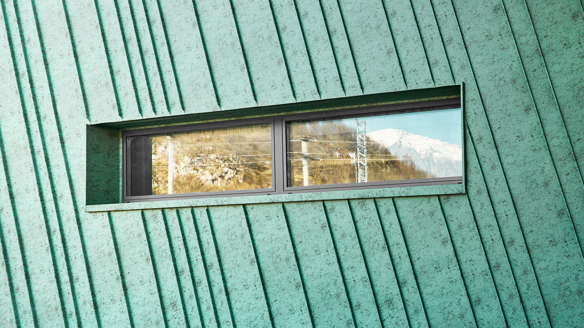 Detail mit leicht schräg verlaufender Fassade mit kleinem, länglichem Fenster, in dem sich Berge und elektrische Leitungen widerspiegeln. Seitenansicht auf Fassade und Glasfront mit Eingang.