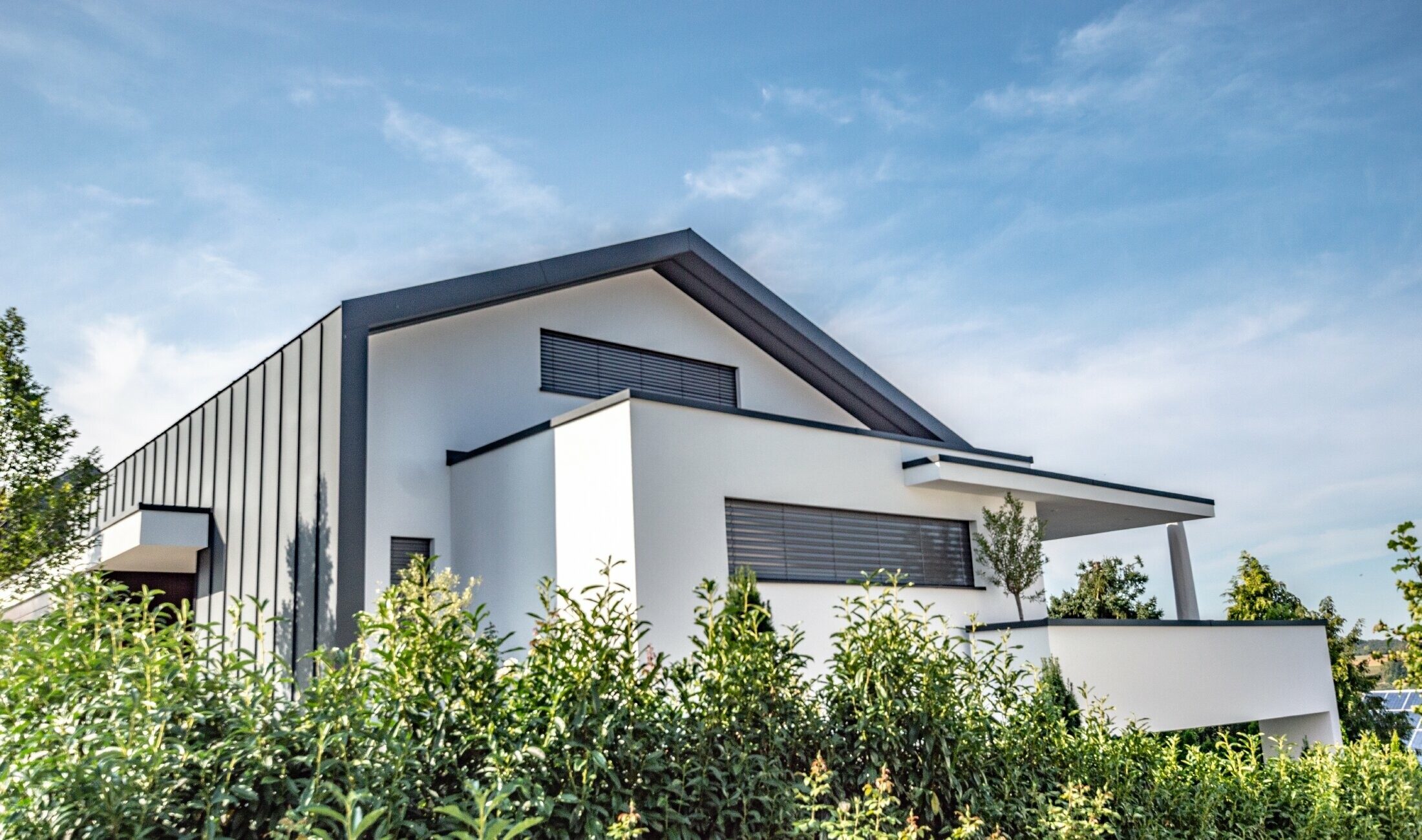 Maison individuelle moderne où la couverture de toit se prolonge sur la façade par agrafage. La couleur du matériau PREFA est l’anthracite.