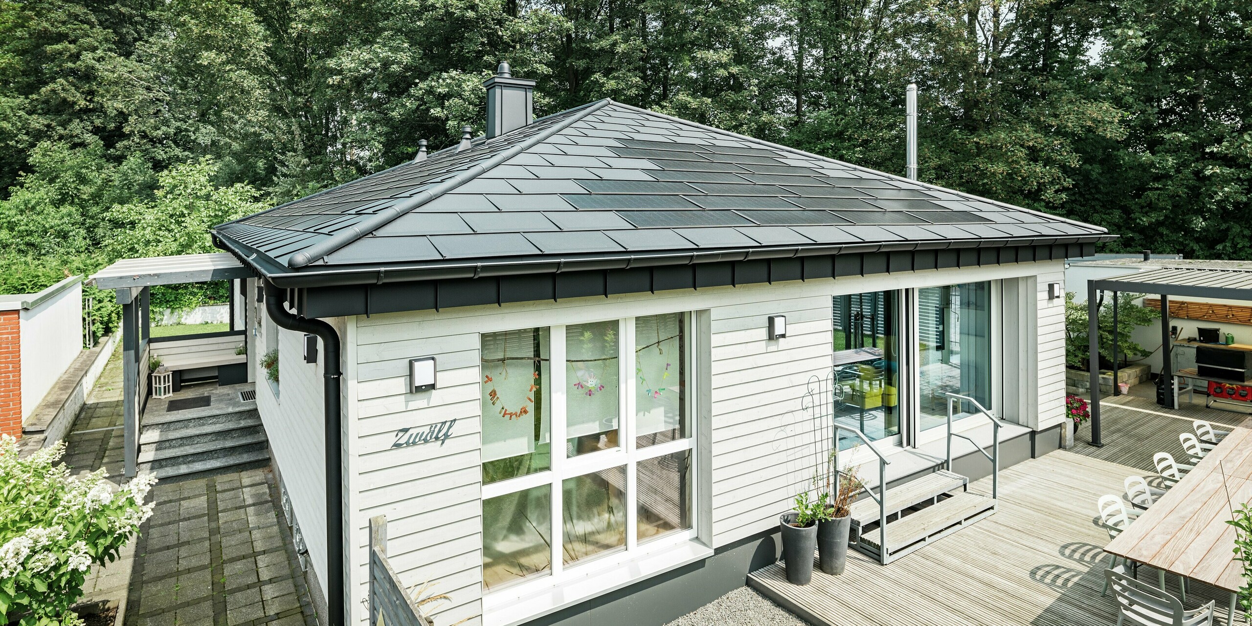 Bungalow moderne à Rommerskirchen avec toit en aluminium PREFA. Les tuiles solaires innovantes PREFA protègent la maison et produisent en même temps de l'électricité à partir de l'énergie solaire durable. Les R.16 offrent une protection supplémentaire. Le système d'évacuation des eaux pluviales avec la gouttière et tuyau de descente assure la fonctionnalité nécessaire. Tous les produits en aluminium PREFA sont dotés d'un revêtement de couleur P.10 noir de haute qualité, garantissant ainsi une apparence générale élégante. 